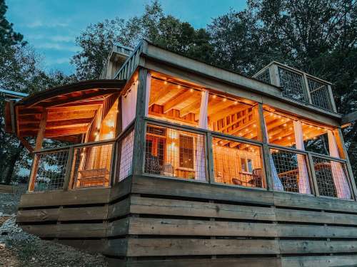 A cozy wooden cabin with warm lights, surrounded by trees, featuring a spacious deck and inviting atmosphere.
