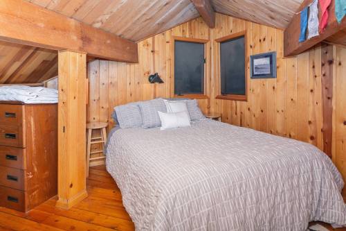 Cozy bedroom with wooden walls, a large bed, and a small chair, featuring a sloped ceiling and two windows.