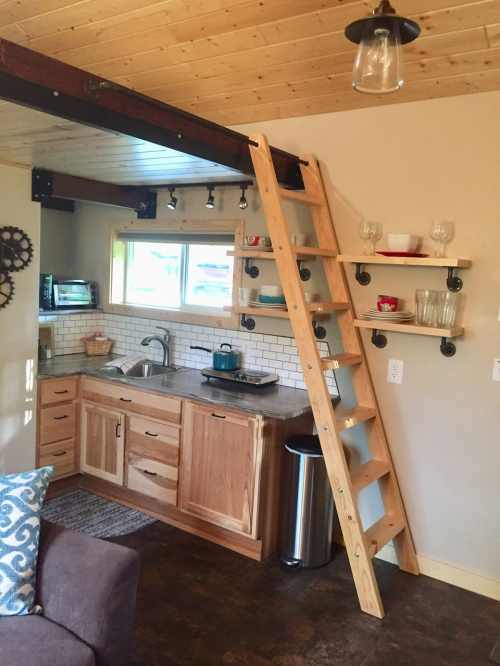 Cozy kitchen with wooden cabinets, a ladder to a loft, and open shelves displaying glassware.