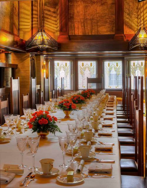 Elegant dining room set for a formal meal, featuring a long table with floral centerpieces and fine tableware.