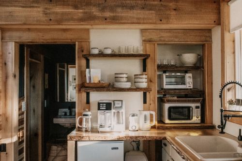 A cozy kitchen with wooden shelves, a sink, and various appliances, featuring a warm, rustic design.