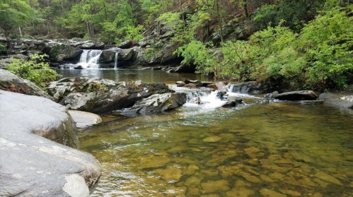 A serene river scene with gentle waterfalls, surrounded by lush greenery and rocky banks.