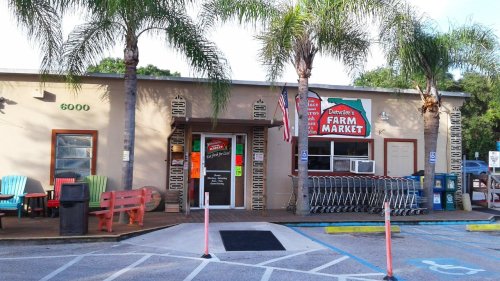 Exterior of Devine's Farm Market featuring palm trees, colorful chairs, and shopping carts outside the entrance.