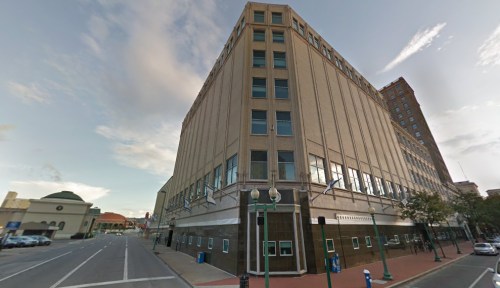 A tall, historic building with large windows, located at a street corner under a blue sky.