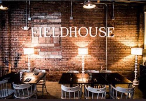 Interior of a restaurant named "Fieldhouse," featuring brick walls and wooden tables with white chairs.