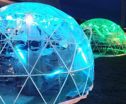 Two illuminated geodesic domes at night, featuring vibrant blue and green lights, set in a grassy area.
