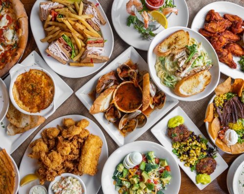 A variety of dishes including seafood, pasta, sandwiches, salads, and fried chicken arranged on white plates.