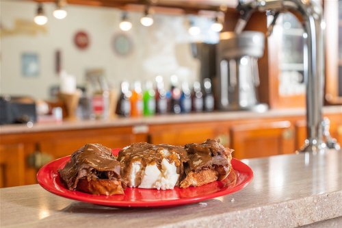 A red plate with three servings of meat and gravy over rice, set on a counter with a blurred bar in the background.
