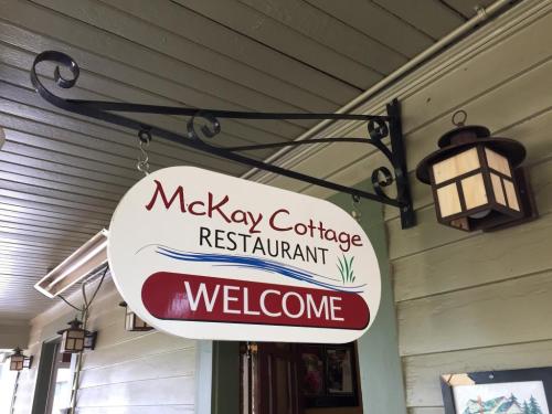 Sign for McKay Cottage Restaurant with "WELCOME" displayed, hanging from a decorative bracket under a lantern.