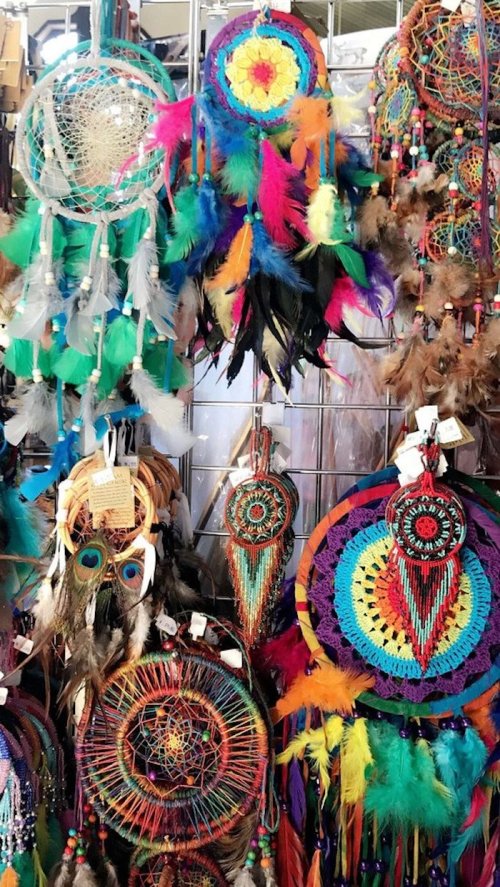 Colorful dreamcatchers with feathers and beads displayed on a rack, showcasing intricate designs and vibrant hues.
