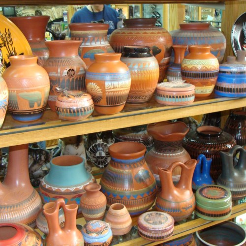 A display of various colorful pottery pieces, featuring intricate designs and patterns, arranged on wooden shelves.