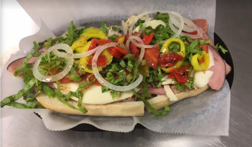A sub sandwich loaded with ham, cheese, lettuce, onions, peppers, and roasted red peppers on a hoagie roll.