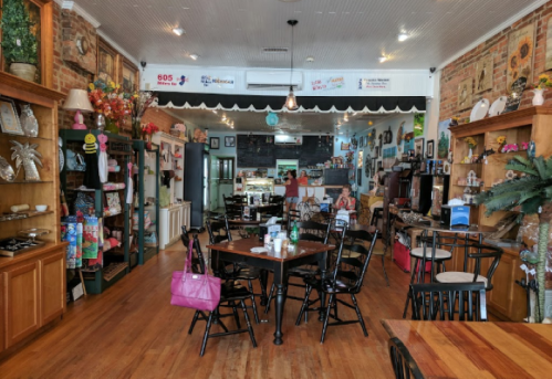 Cozy café interior with wooden tables, chairs, and colorful decor, featuring shelves of items and a welcoming atmosphere.