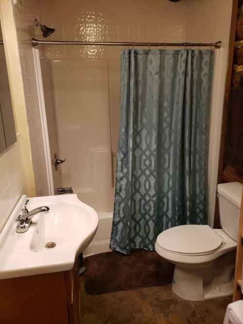 A small bathroom featuring a shower with a blue curtain, a sink, and a toilet on a tiled floor.