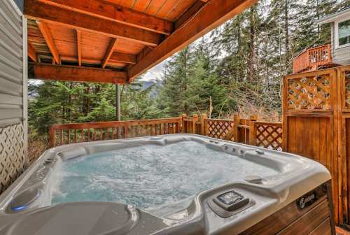 A hot tub on a wooden deck surrounded by trees and a mountain view, under a covered patio.