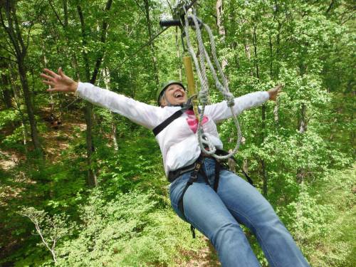 A person joyfully zip-lining through a lush green forest, arms outstretched and smiling.
