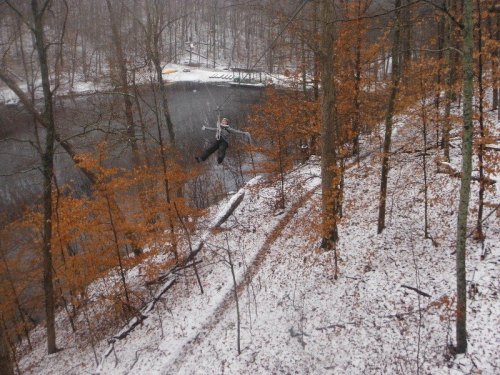A snowy forest scene with orange leaves, a pond, and a person zip-lining through the trees.