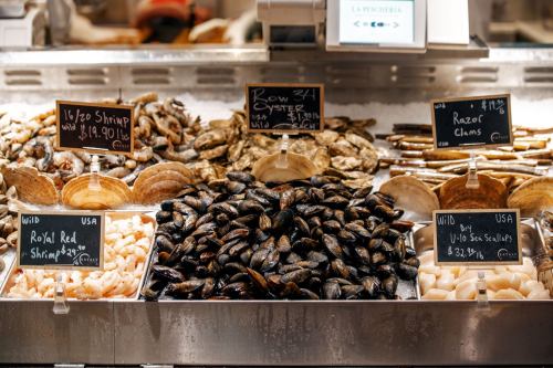 A seafood display featuring shrimp, oysters, clams, and scallops with price tags on a market counter.