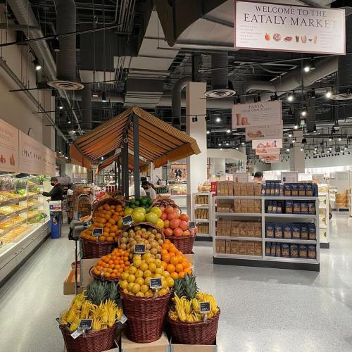 A vibrant display of fresh fruits in baskets at Eataly Market, with shelves of pasta and other products in the background.