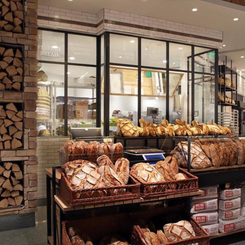 A bakery display featuring various artisanal breads in baskets, with a glass case showcasing more baked goods.