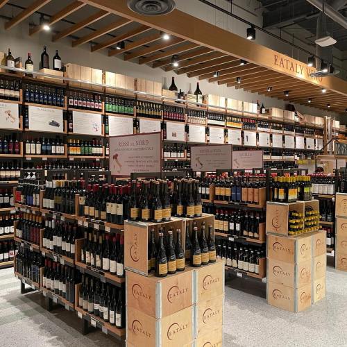A wine display at Eataly featuring shelves filled with various bottles and wooden crates in a well-lit store.