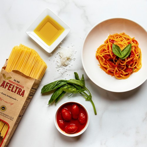 A plate of spaghetti with tomato sauce and basil, surrounded by pasta, olive oil, cherry tomatoes, and grated cheese.