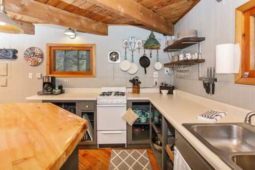 Cozy kitchen with wooden beams, a gas stove, and open shelving displaying utensils and dishware.