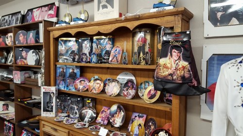 A wooden display shelf filled with various Elvis memorabilia, including plates, photos, and a black jumpsuit.