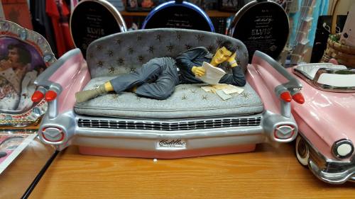 A decorative figurine of a man lounging on a pink Cadillac-themed couch, reading papers.