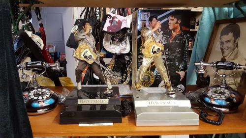 Two Elvis Presley figurines with guitars on display, alongside vintage-style telephones and memorabilia.