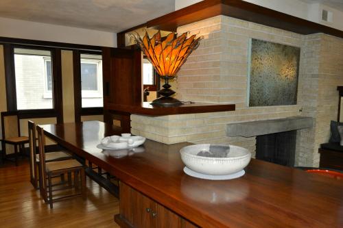 A modern kitchen with a wooden table, decorative lamp, and a stone fireplace, featuring minimalist decor and natural light.