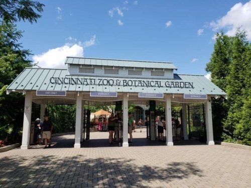 Entrance to the Cincinnati Zoo & Botanical Garden, featuring a green roof and clear blue sky. Visitors are entering.