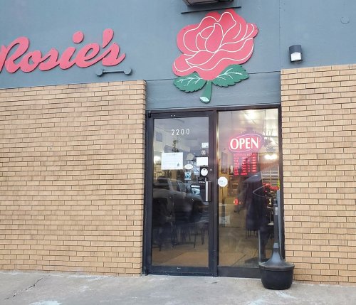 Exterior of Rosie's restaurant featuring a rose logo and an "OPEN" sign on the door. Brick facade.