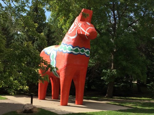 A large, colorful wooden horse statue stands in a park surrounded by trees.