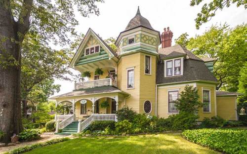A charming yellow Victorian house with a turret, surrounded by lush greenery and a well-maintained garden.