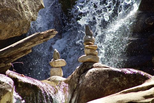 Two stone cairns balanced on rocks near a waterfall, with water cascading in the background.