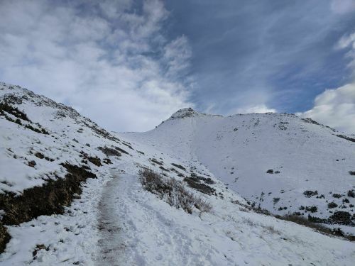 A snowy mountain landscape with a winding path leading up to a peak under a cloudy sky.