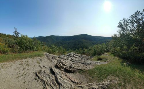 A panoramic view of rolling green hills under a clear sky, with rocky terrain in the foreground.