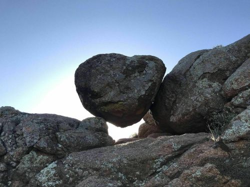 A large heart-shaped rock balanced between two boulders against a clear blue sky.