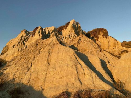 Golden-hued rock formations under a clear blue sky, with sparse vegetation on the peaks.
