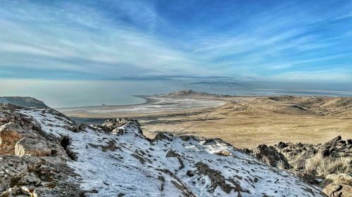 A panoramic view of a vast, snowy landscape with a distant shoreline under a blue sky.