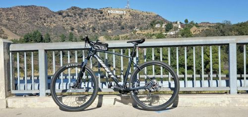 A mountain bike parked on a bridge with the Hollywood sign visible in the background on a sunny day.
