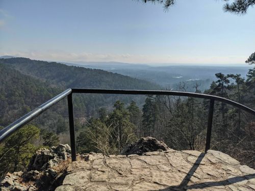 A scenic view from a rocky overlook, featuring rolling hills and a clear blue sky.