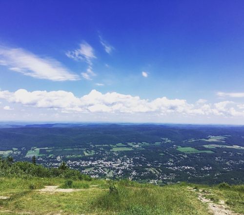 A panoramic view of a green valley and small town under a bright blue sky with fluffy white clouds.