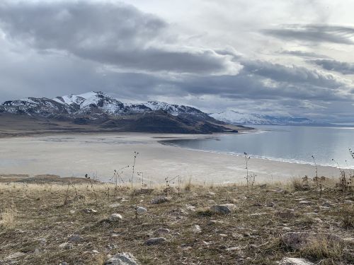 A scenic view of a beach with mountains in the background under a cloudy sky.