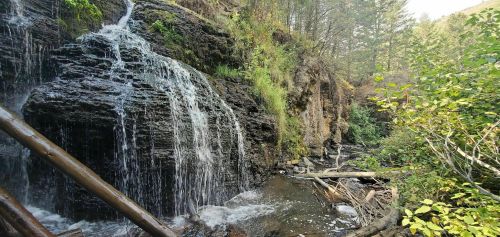 A serene waterfall cascading over rocky terrain, surrounded by lush greenery and trees in a peaceful natural setting.