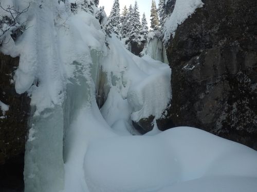 A snowy landscape with icy formations and a narrow path between rocky cliffs, surrounded by evergreen trees.
