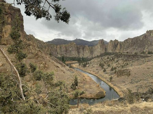 A winding river flows through a rocky canyon landscape under a cloudy sky, surrounded by sparse vegetation.