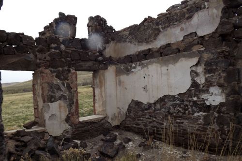 Interior of a dilapidated stone building with crumbling walls and exposed brick, surrounded by grassy landscape.