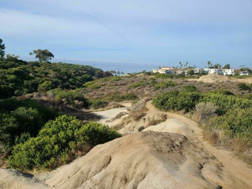 A scenic landscape featuring rocky terrain, lush greenery, and distant coastal views under a clear blue sky.